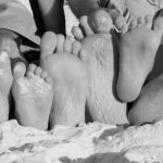 black and white photo of family feet in sandy beach